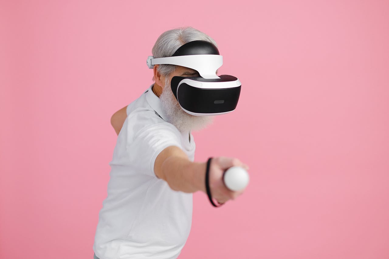 category-03 Senior man wearing VR headset and interacting with virtual environment against pink background.